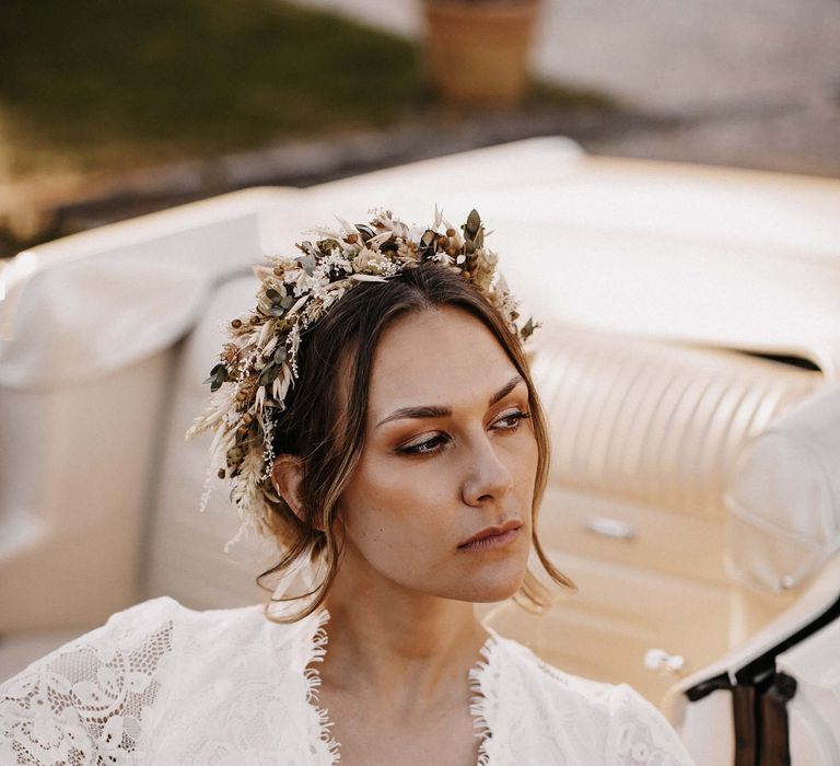 Boho bride in a lace wedding dress with V front neckline wearing a dried flower crown sitting in her wedding car 