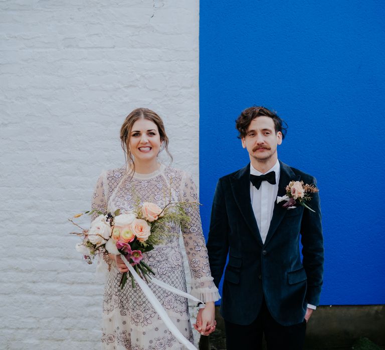 Bride & groom stand in front of two toned blue wall for couples portraits 