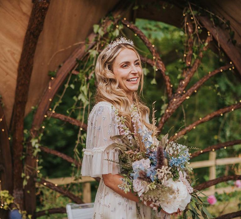 Bride golden crown with pearl embellishment whilst holding large floral bouquet complete with pastel blue florals and white flowers with green foliage