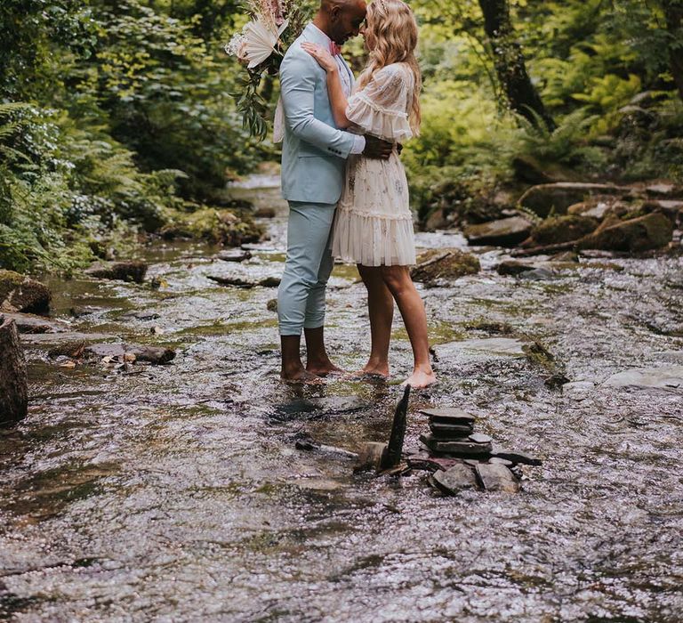 Bride & groom stand within the woodland as they go barefoot across pebbles and water