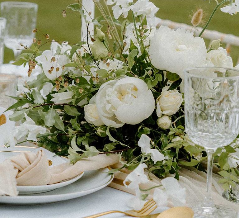 White and green wedding flower centrepiece with gold cutlery, taper candles and linen napkins 