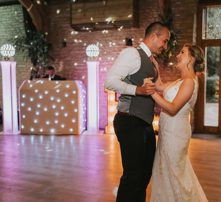 Bride in lace Justin Alexander Wedding dress and groom in white shirt, grey waistcoat and pink tie have their first dance at Tythe Barn wedding with barn wedding flowers