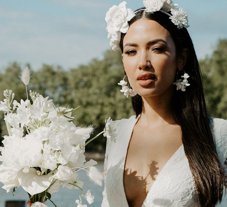 Bride in a lace wrap wedding dress holding an all white bouquet and wearing a flower headband and hoop earrings 