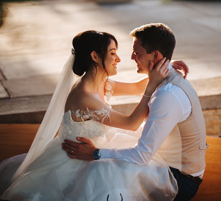 Bride & groom wrap their arms around one another on wedding day as the sun sets