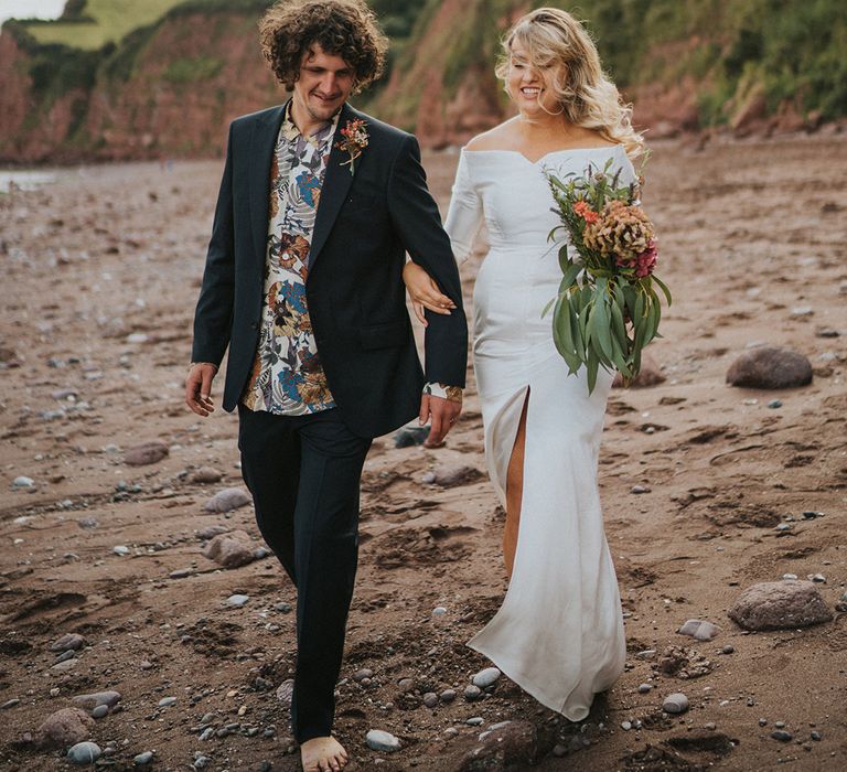 Bride & groom walk along the beach on their wedding day