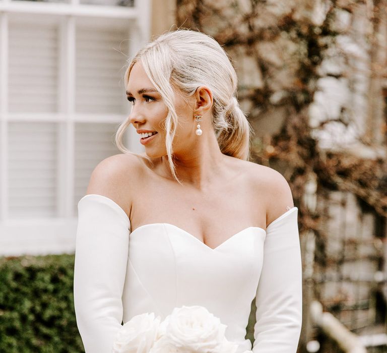 Beautiful bride in a fitted strapless wedding dress with detachable long sleeves holding a white rose wedding bouquet 