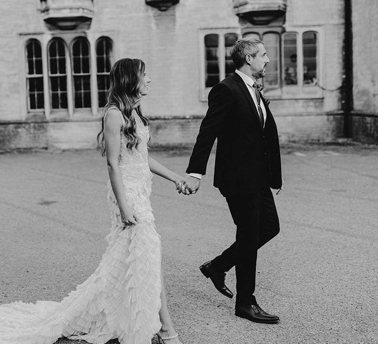 Black & white image of bride and groom walking hand in hand