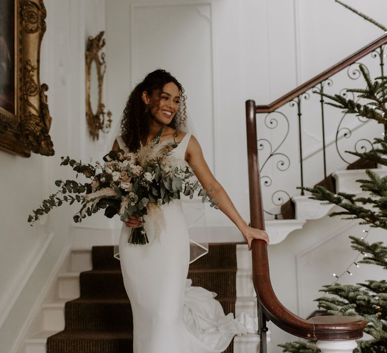 Bride walks down staircase on her wedding day whilst holding bridal bouquet 