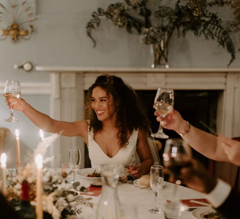 Bride & groom during wedding reception as bride lifts wine glass in celebration