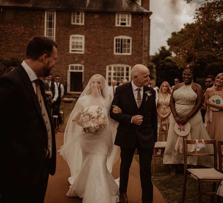 Father of the bride walking his daughter down the aisle in a lace wedding dress and veil 