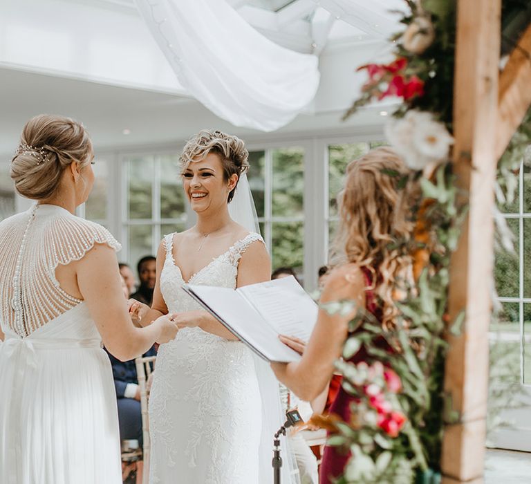 Brides hold hands and smile at one another during wedding ceremony