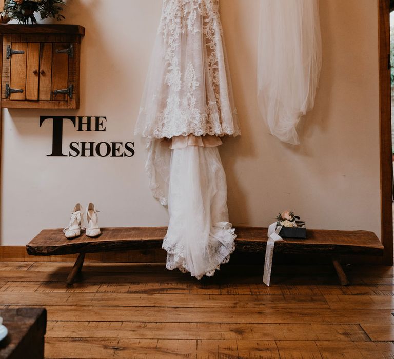 Lace wedding dress with train hands from wooden beam next to veil, shoes and bouquet at the Tythe Barn 