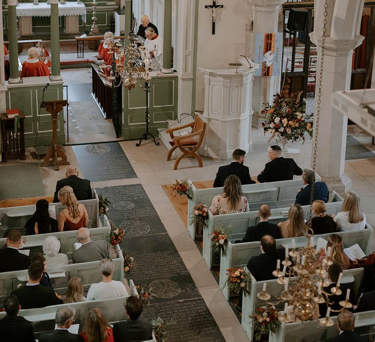 Guests wait at church for bride and groom to arrive with Autumnal flowers