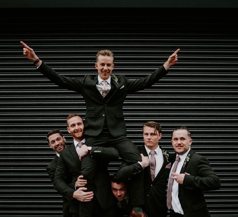 Groom is held up by his groomsmen on their wedding day