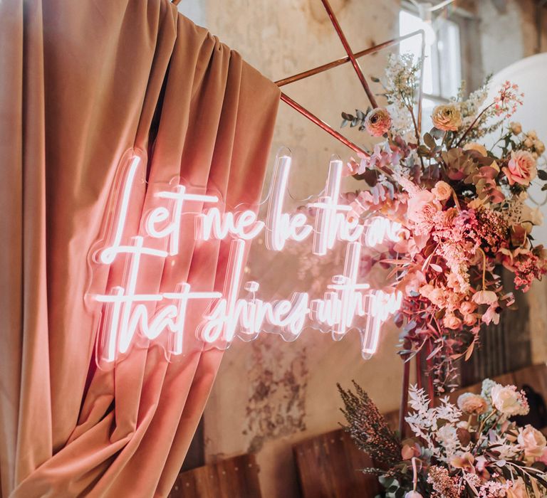 Pink neon wedding sign on copper frame arch with pink draping and mixed flower clouds