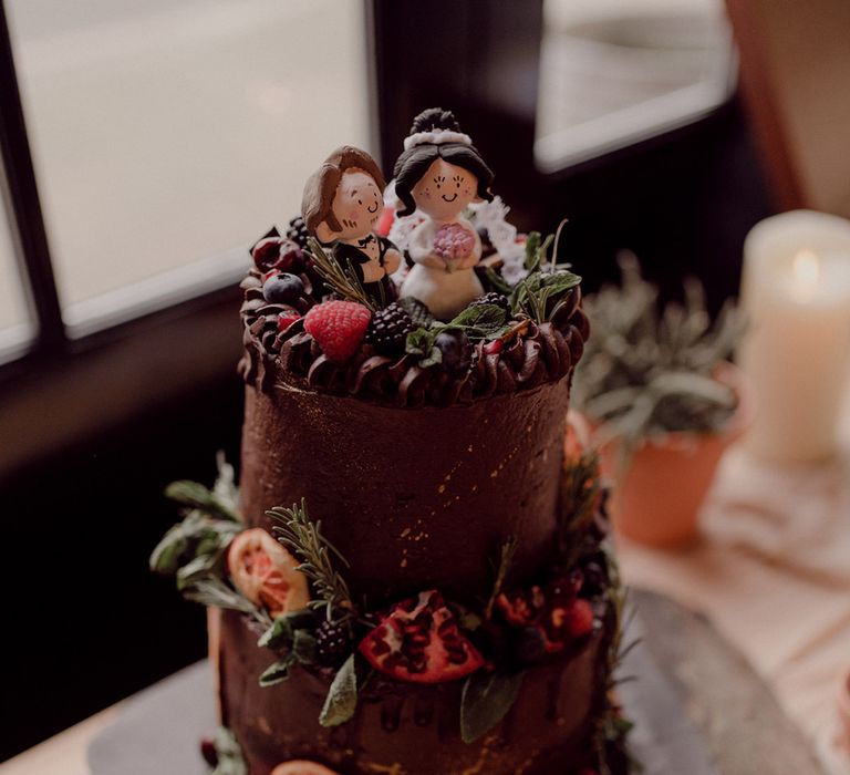 Two-tier vegan chocolate cake with fresh berries and dried oranges and pomegranate with handmade custom cake topper