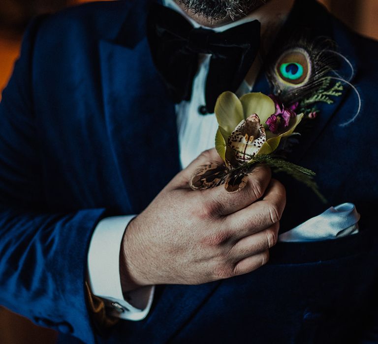 groom affixes his large tropical boutonnière with peacock feather