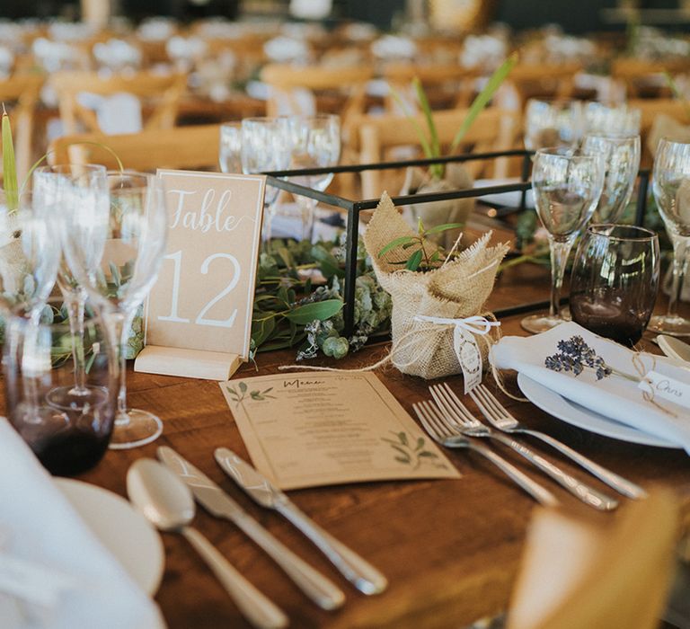 Brown card menus and brown table number signs with wedding plant favours for guests on wooden table for table setting 