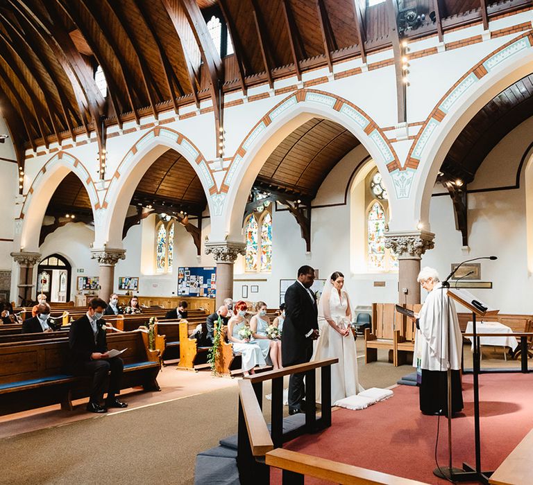 Bride and groom stand at the altar of their church wedding ceremony with small number of guests