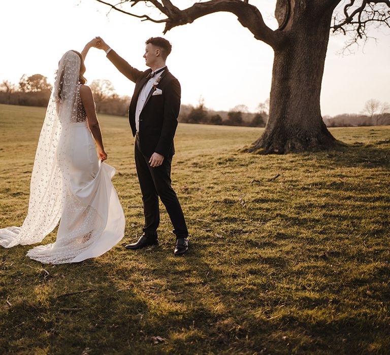 Groom in black tie spins the bride around outside in the grounds of Burley Manor 