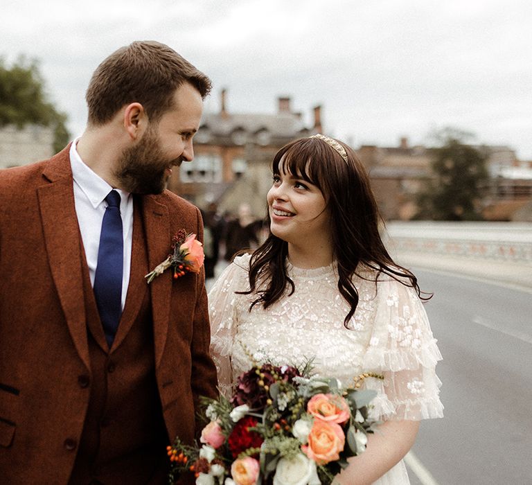 Bride and groom look at each other adoringly with brie holding pink, white and red wedding bouquet