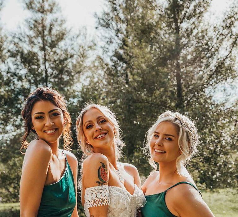 Bridesmaid in emerald green satin bridesmaid dresses with bride in boho wedding dress and bright bouquets