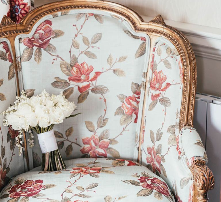 Blue floral armchair with gold detail with white bridal bouquet of roses