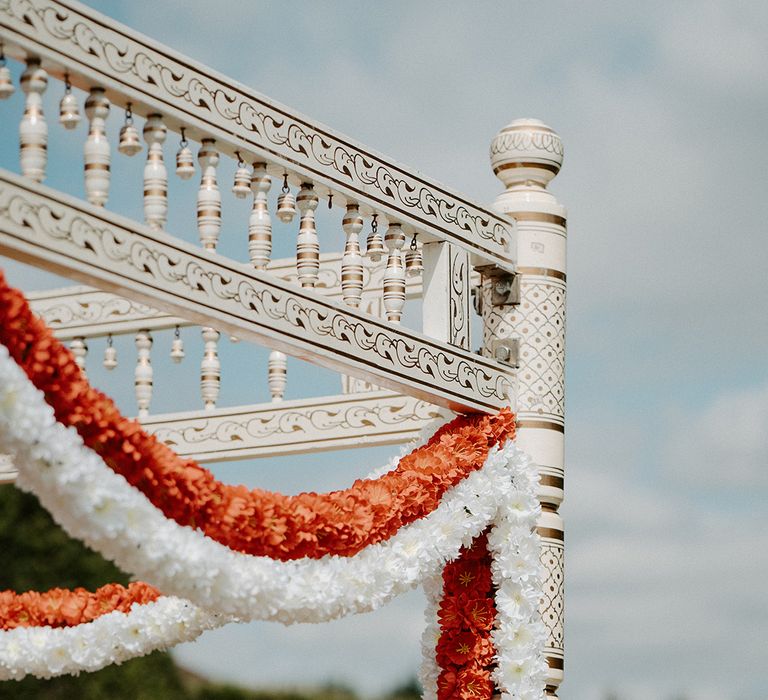 Colourful florals in orange and white hang outdoors for multicultural wedding day at the Lillibrooke Manor And Barns