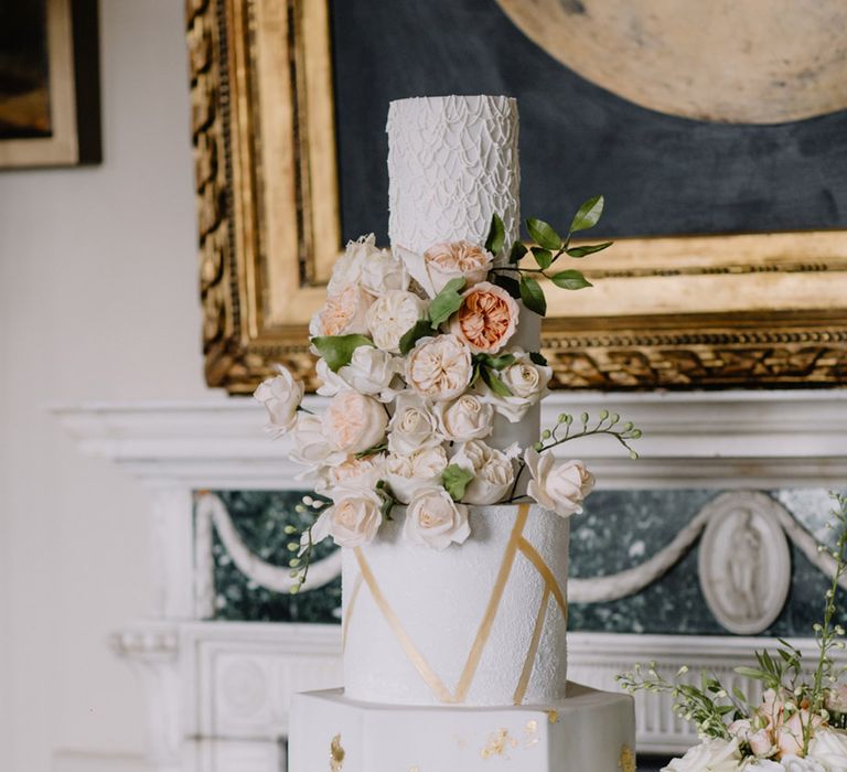 Four tier wedding cake with hexagonal base cake layer with gold details and geometric patterns decorated with flowers 