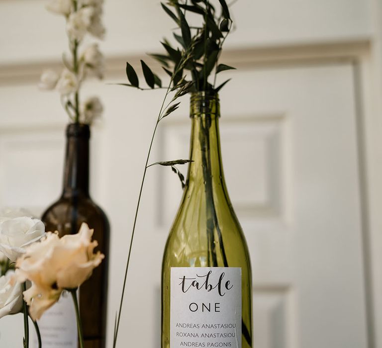 Wine glass filled with pink flower and green foliage complete with Table One label stood on wooden table