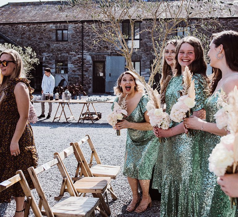 Bridesmaids stand and look happy in their sequin green dresses holding dried flower bouquets for the outdoor ceremony 