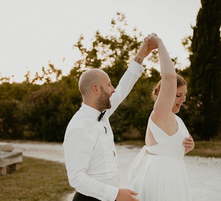 Groom wears white shirt and black bow tie whilst spinning his bride around who wears London Halfpenny wedding dress