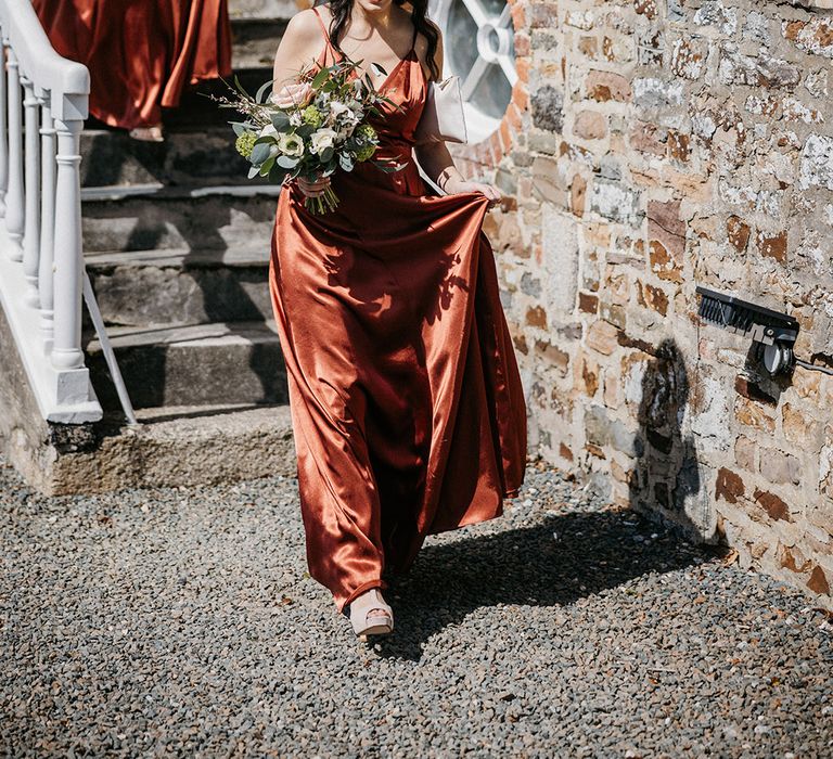 Bridesmaids in orange satin dresses walk down the stairs for the wedding 