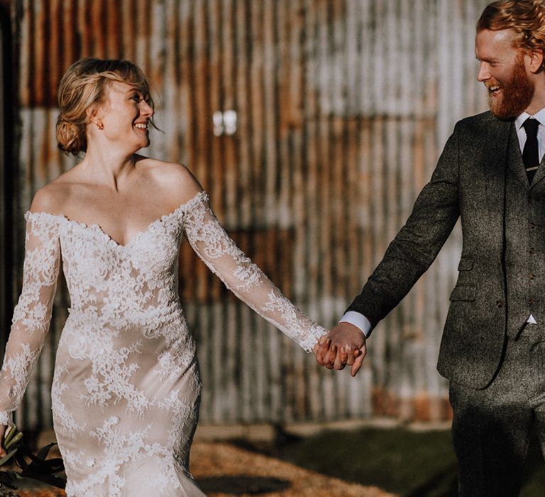 Bride and groom walk holding hands during their windy wedding day 