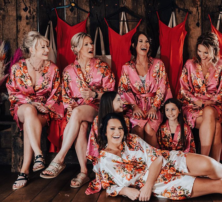 Bridesmaids and flower girls in matching oink floral robes with the bride in a white and orange floral robe as they get ready together