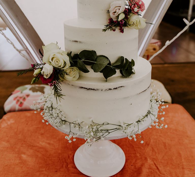 Three tier naked wedding cake with white frosting and floral decor 