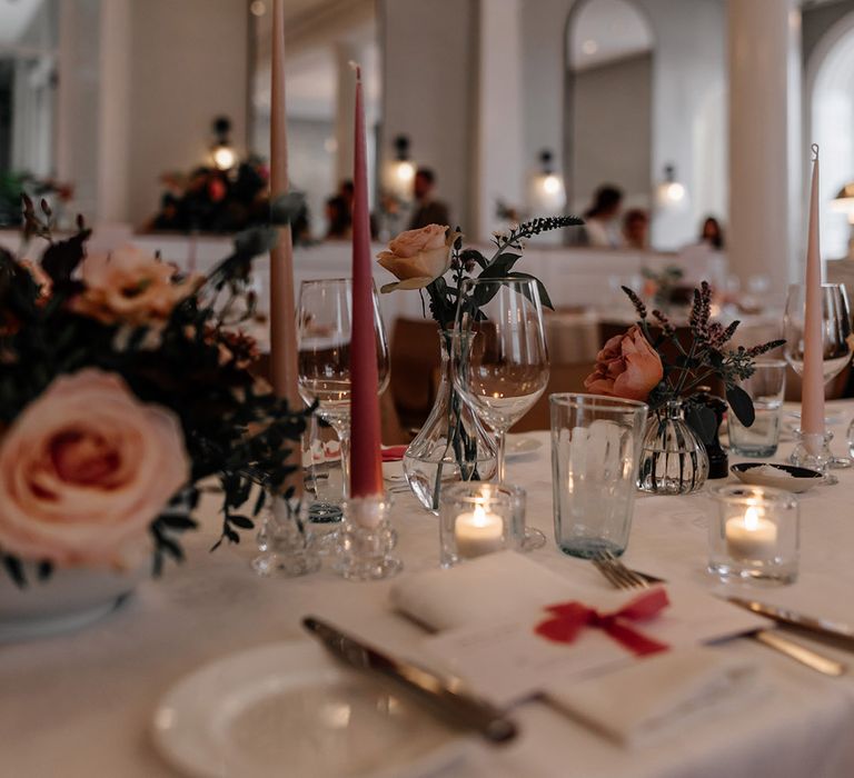 Neutral wedding tablescape with pink dinner candles and foliage decorations with pink flowers