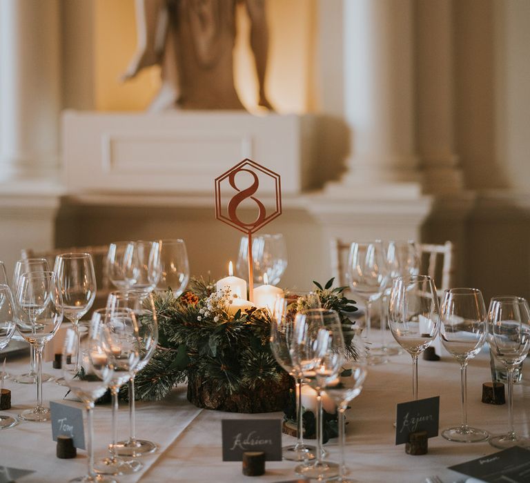 Greenery wedding centrepiece with pillar candles and wooden table number 