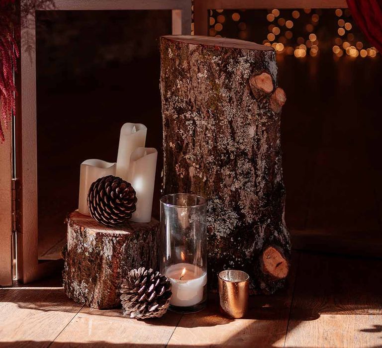 Two natural tree trunks with large pinecone decor, pillar candles, large glass candle jars and golden candle sticks