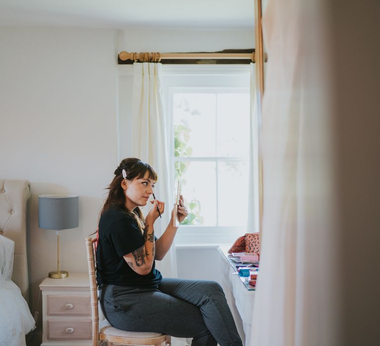 Bride in leather-look black jeans and black t shirt doing makeup before wedding