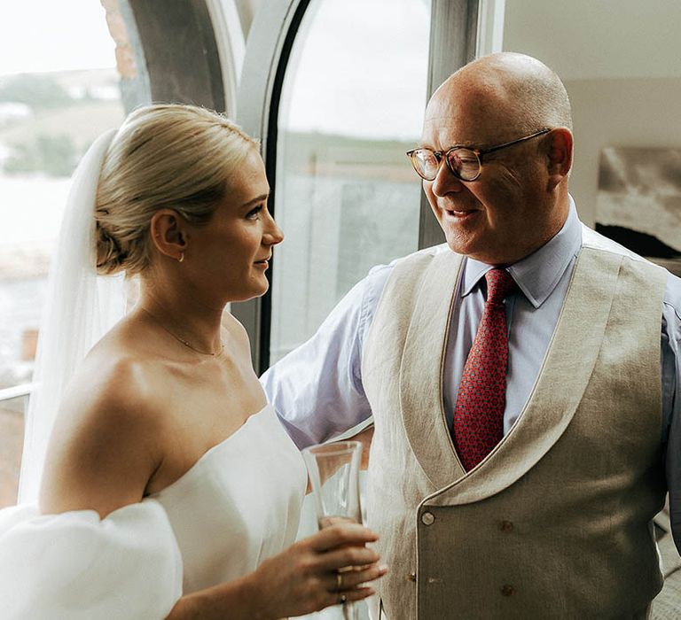 Bride wears puffed sleeve Jesus Peiro wedding dress and speaks to her father in cream waistcoat and red tie