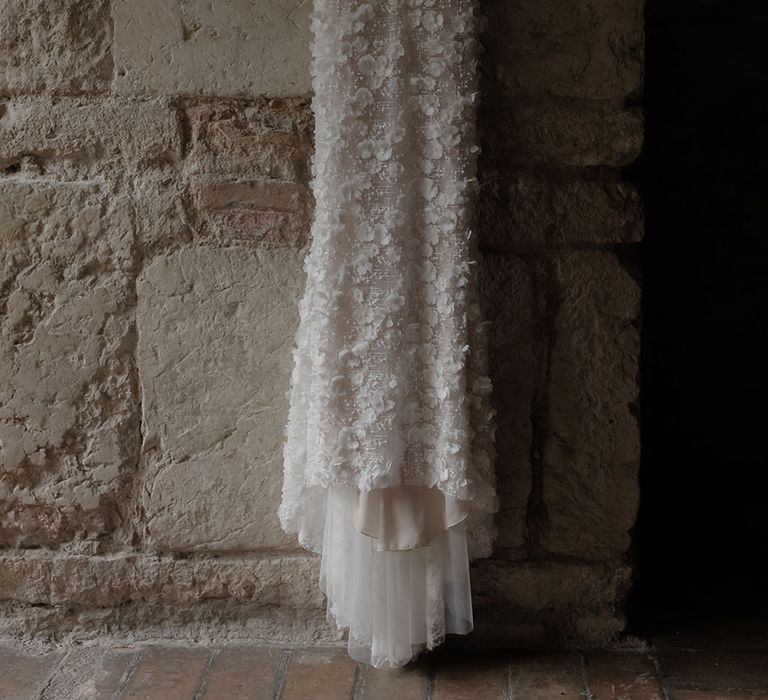 Appliqué Pronovias wedding dress hangs against exposed brick wall 