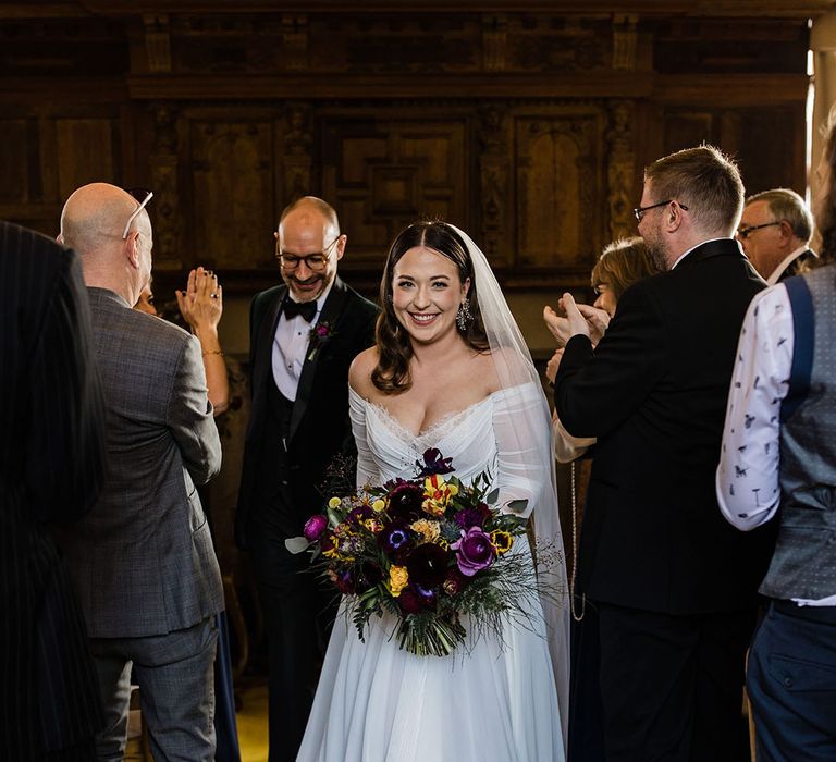 Bride in a off the shoulder long sleeve wedding dress leads the groom back down the aisle as they exit their ceremony as a married couple 