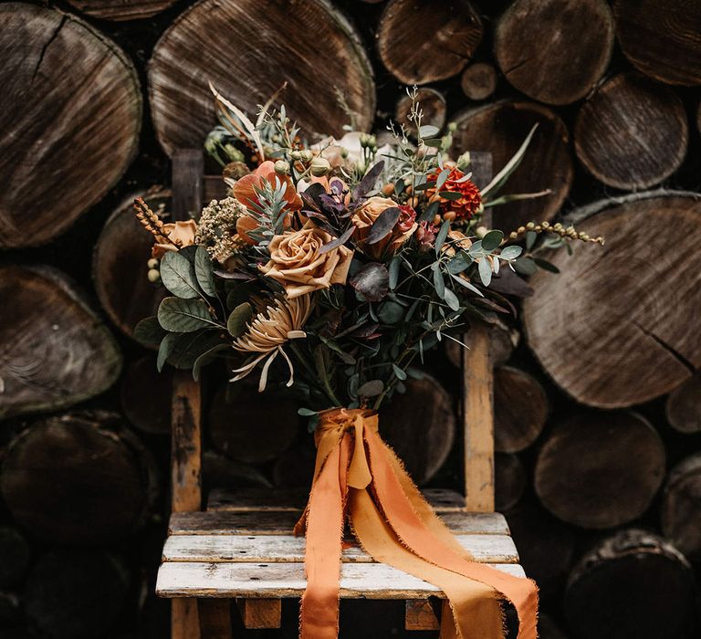 Autumnal styled dried floral bouquet with green foliages and tied with raw edge orange ribbon