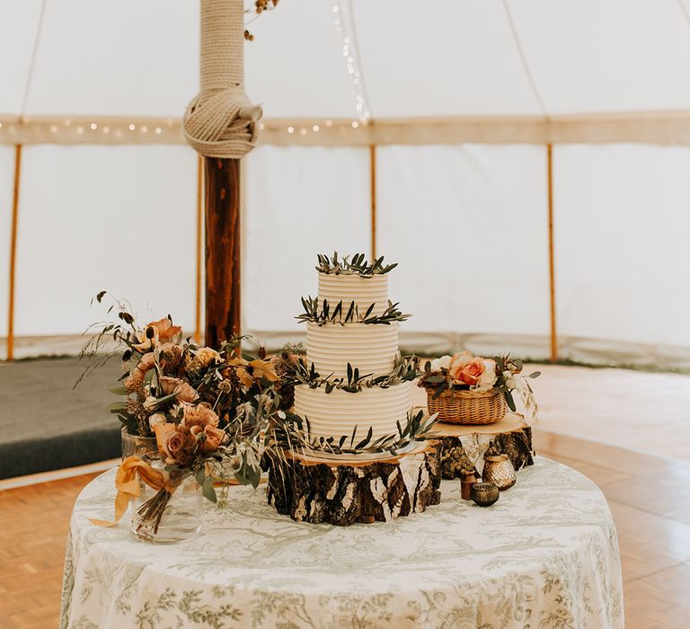 Three tier white frosted wedding cake on a wooden tree trunk cake stand with disco balls and festoon lighting hanging above 