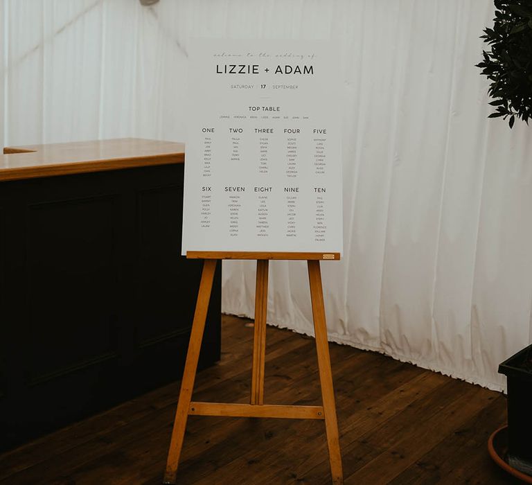 Black and white wedding seating chart on wooden easel inside the white marquee wedding reception 