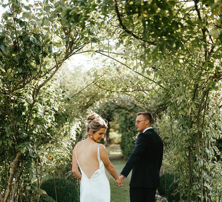 Elms Barn wedding with the bride in a white satin slip wedding dress with low back detail walking out in the grounds with the groom in black tie 