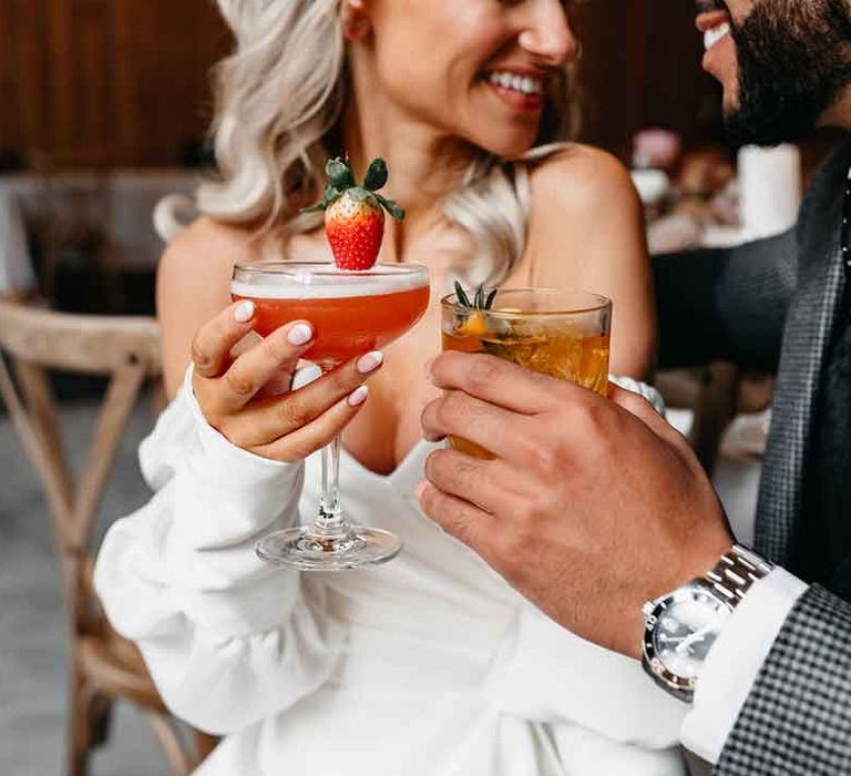 Bride in off the shoulder wedding dress and groom in dark grey blazer and silver watch groom accessory having colourful wedding cocktails at Lodge Farm wedding venue 