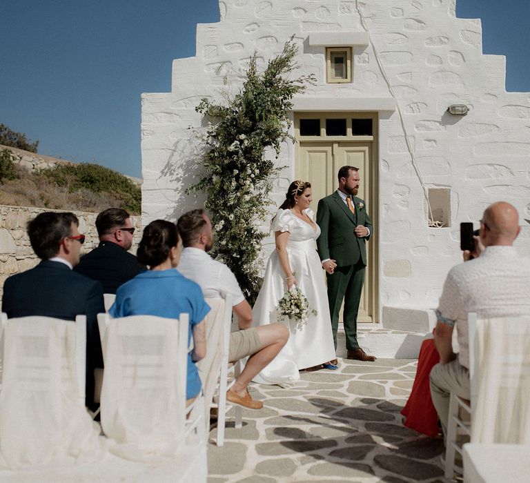 Bride and groom at altar with green and white floral decor during intimate wedding ceremony in Paros