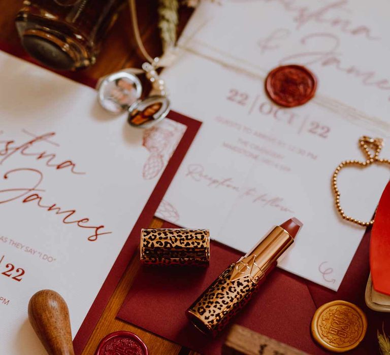 Leopard print lipstick, red wax seals and red and white homemade wedding stationery on wooden floor 